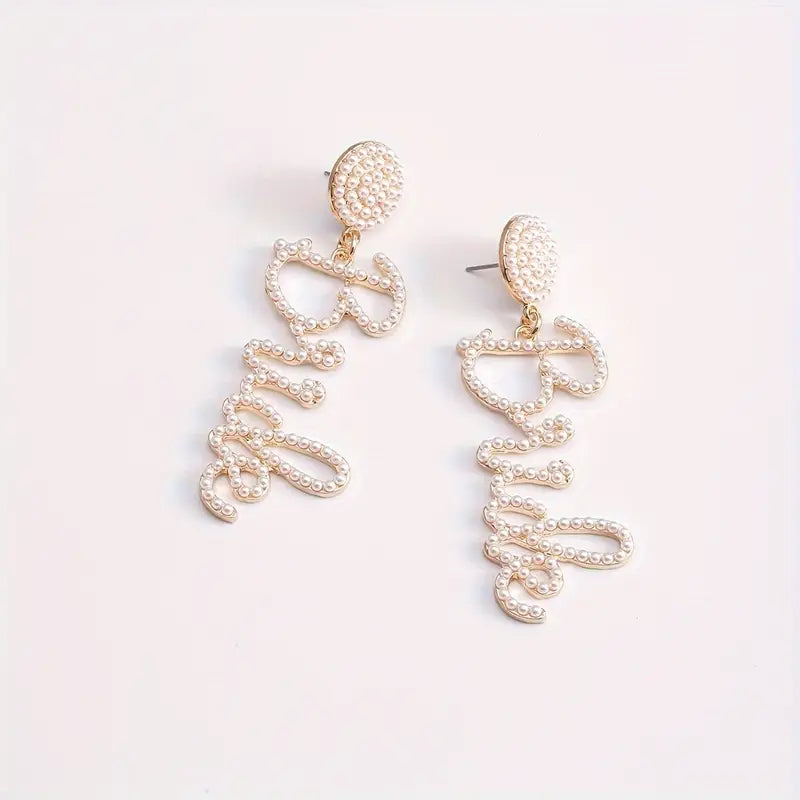 A pair of gold-tone pearl drop earrings with the word 'Bride' written in script.