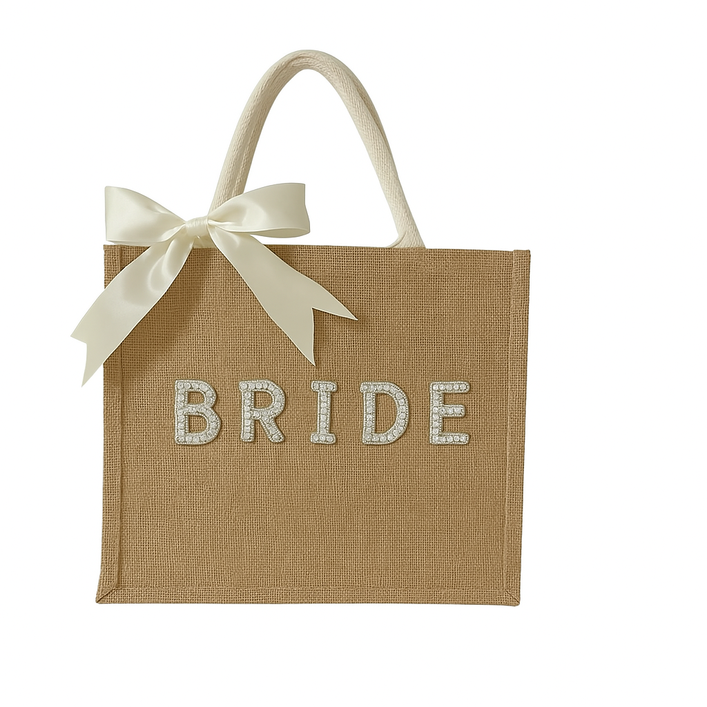 A rectangular burlap tote bag with sturdy cream-colored handles and a large ivory satin bow tied on one side. The front of the bag features the word “BRIDE” spelled out in bold, pearl-embellished letters. The bag is displayed against a plain white background.