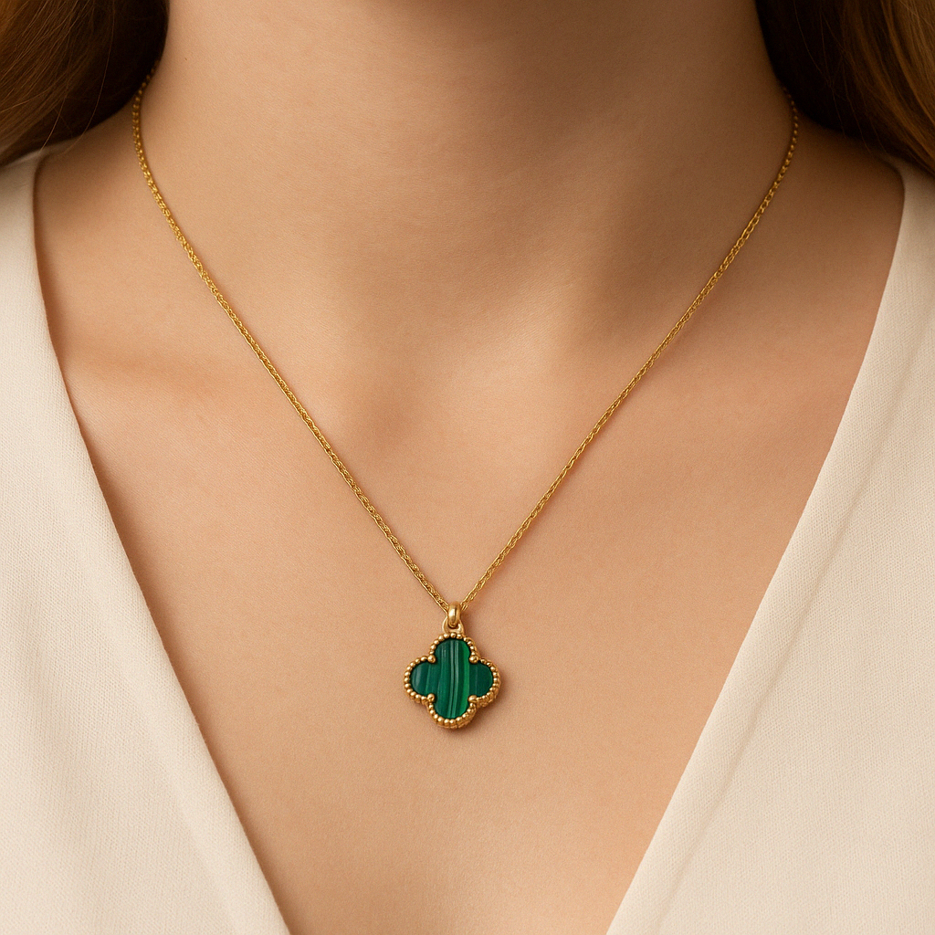 Close-up view of a woman’s neck wearing a gold chain necklace with a green malachite clover-shaped pendant, centered just below her collarbone.