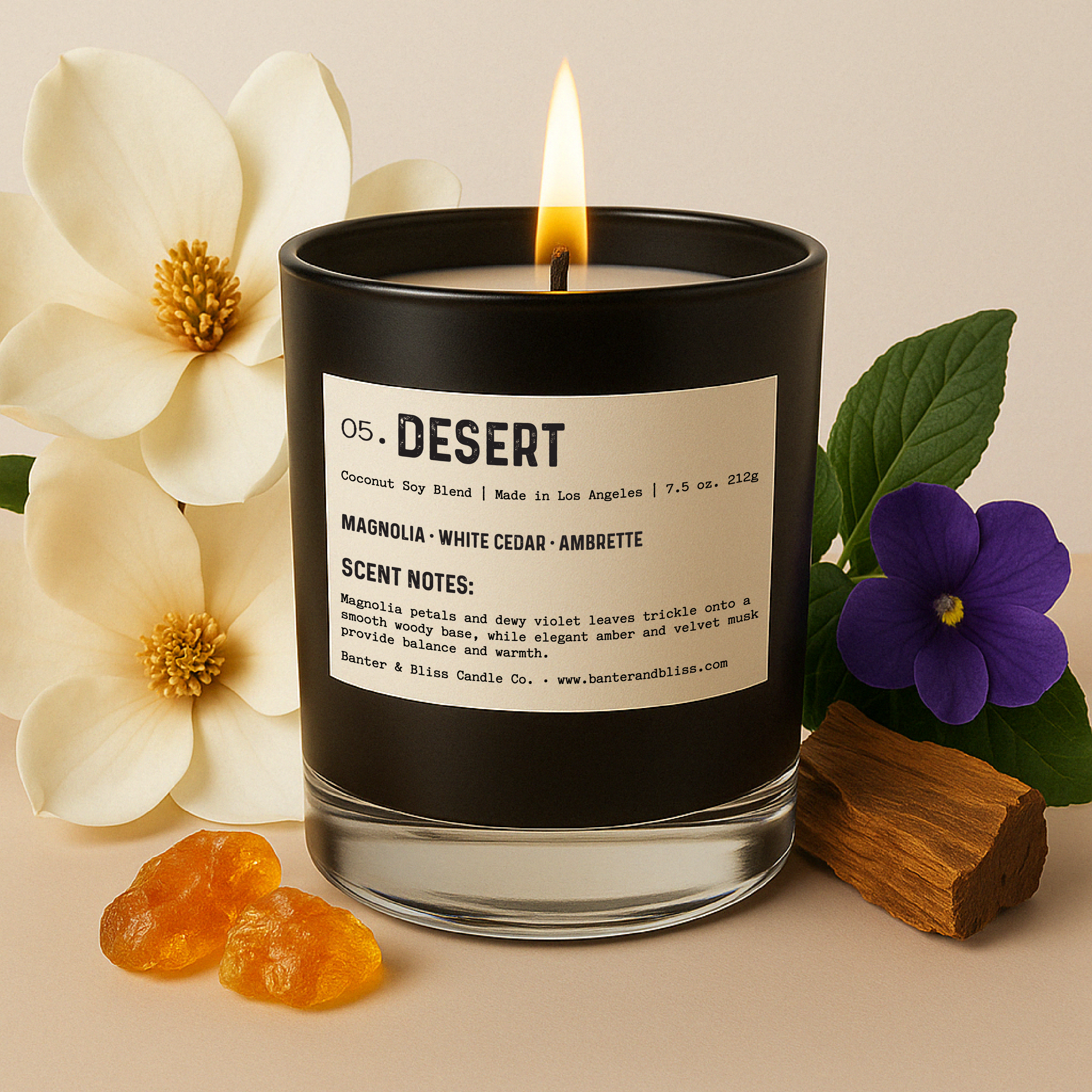 Lit black candle labeled “05. DESERT” surrounded by realistic magnolia flowers, violet blossom, green leaves, amber resin pieces, and a piece of cedar wood. Set against a soft pastel background for a warm, natural aesthetic.
