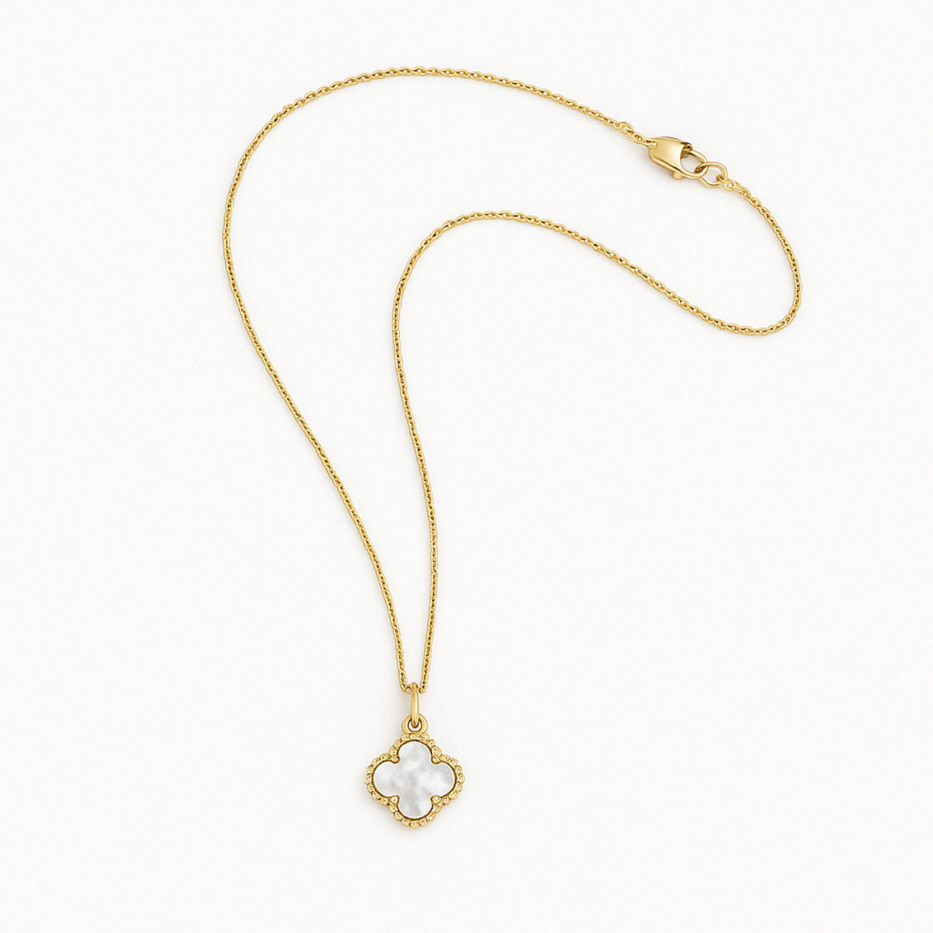 A product photo of a gold necklace laid flat on a white background. The necklace features a clover-shaped mother-of-pearl pendant with a beaded gold edge and a fine gold chain, arranged in a natural curve with the clasp visible at the top.