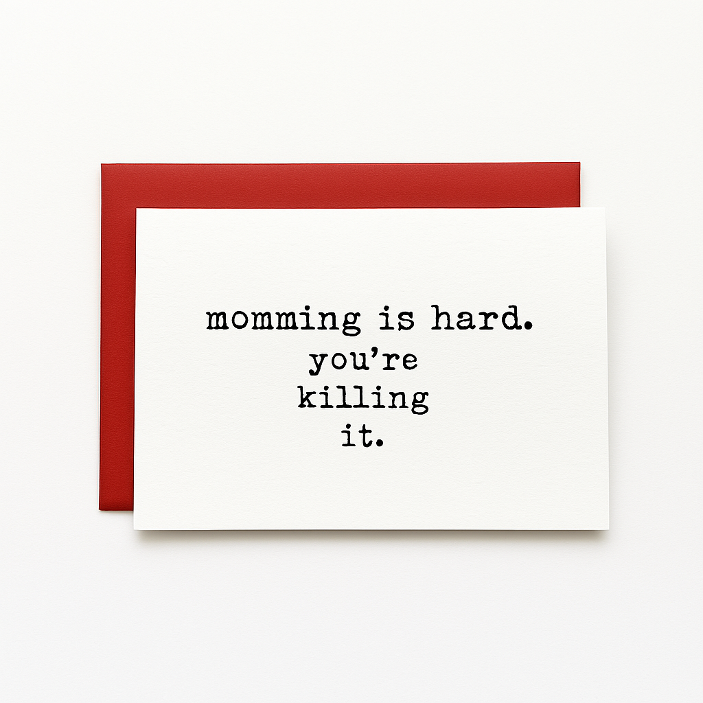 White greeting card with black typewriter-style text that reads 'momming is hard. you're killing it.' centered on top of a red envelope, both placed against a plain white background.