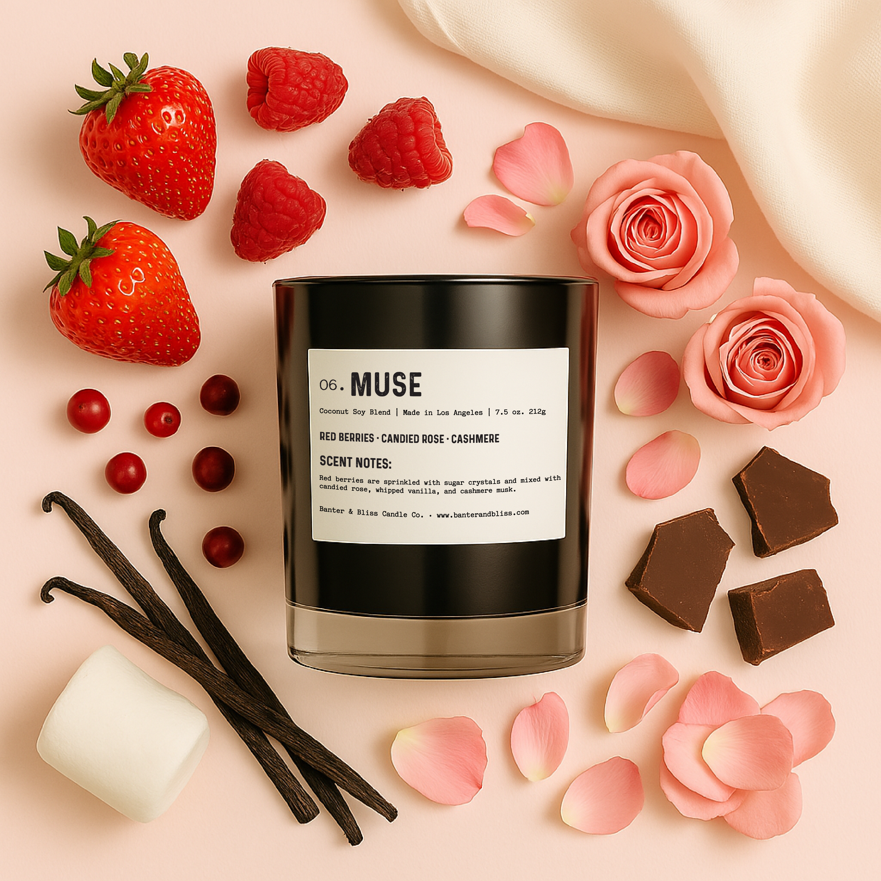 A flat lay image featuring a black candle labeled "06. MUSE" surrounded by ingredients that represent its fragrance notes. These include fresh strawberries, raspberries, red berries, pink rosebuds and petals, vanilla beans, chocolate pieces, and a white marshmallow. The background is a soft pastel pink fabric, and the overall lighting is warm and professional, giving the photo a luxurious, high-end feel.