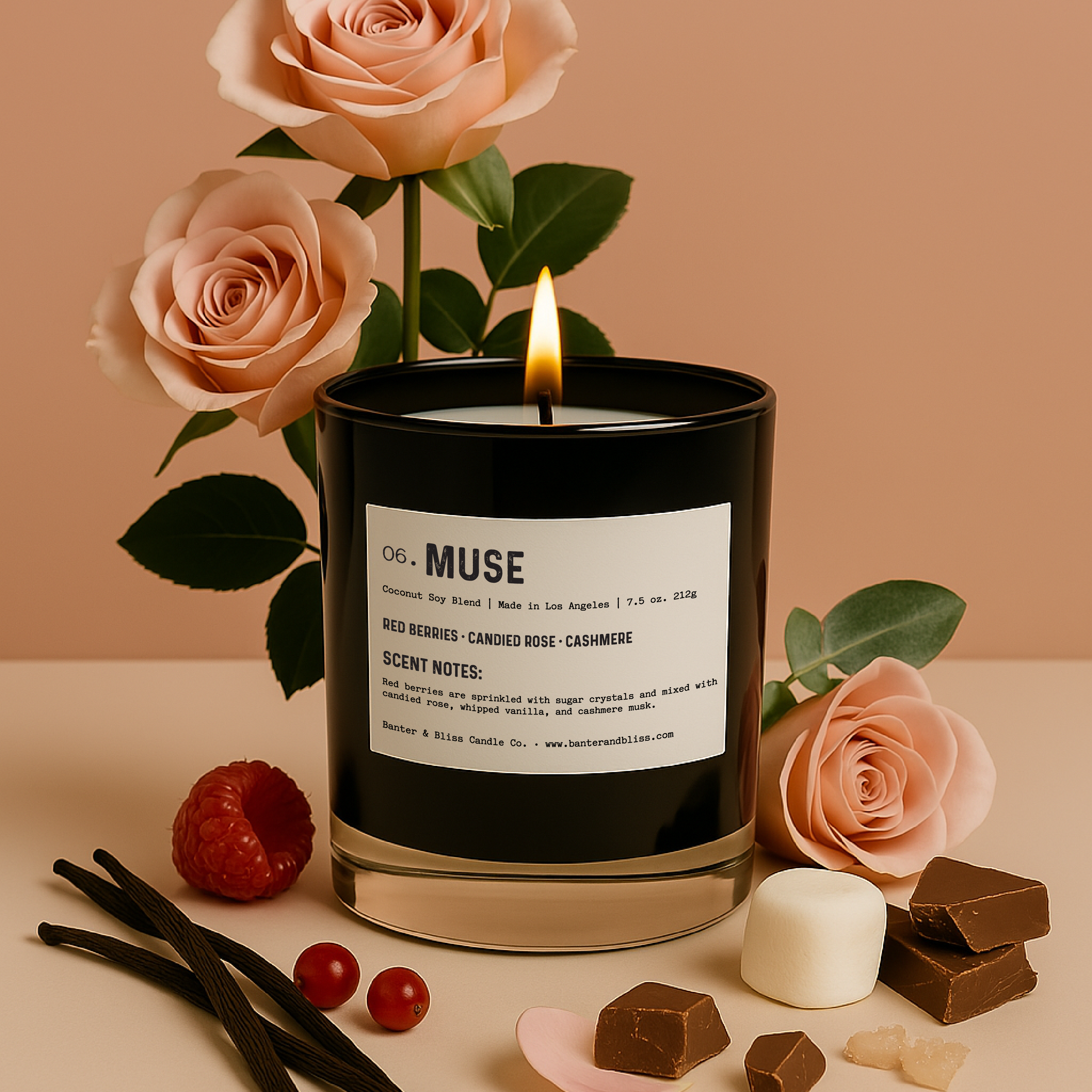 A professionally styled image featuring a black candle labeled "06. MUSE" surrounded by blush pink roses, red berries, vanilla pods, chocolate chunks, a marshmallow, and sugar crystals. The candle is lit and positioned against a soft peach background with the roses adding vertical height in the back. The arrangement evokes a romantic and luxurious mood, showcasing the candle’s fragrance notes: red berries, candied rose, whipped vanilla, creamy cocoa, and cashmere musk.