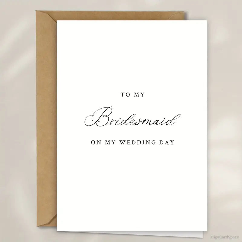 Minimalist white wedding card with a brown envelope behind it, set against a white background. The card reads 'TO MY Bridesmaid ON MY WEDDING DAY' with 'Bridesmaid' written in elegant cursive script and the rest in a classic serif font.