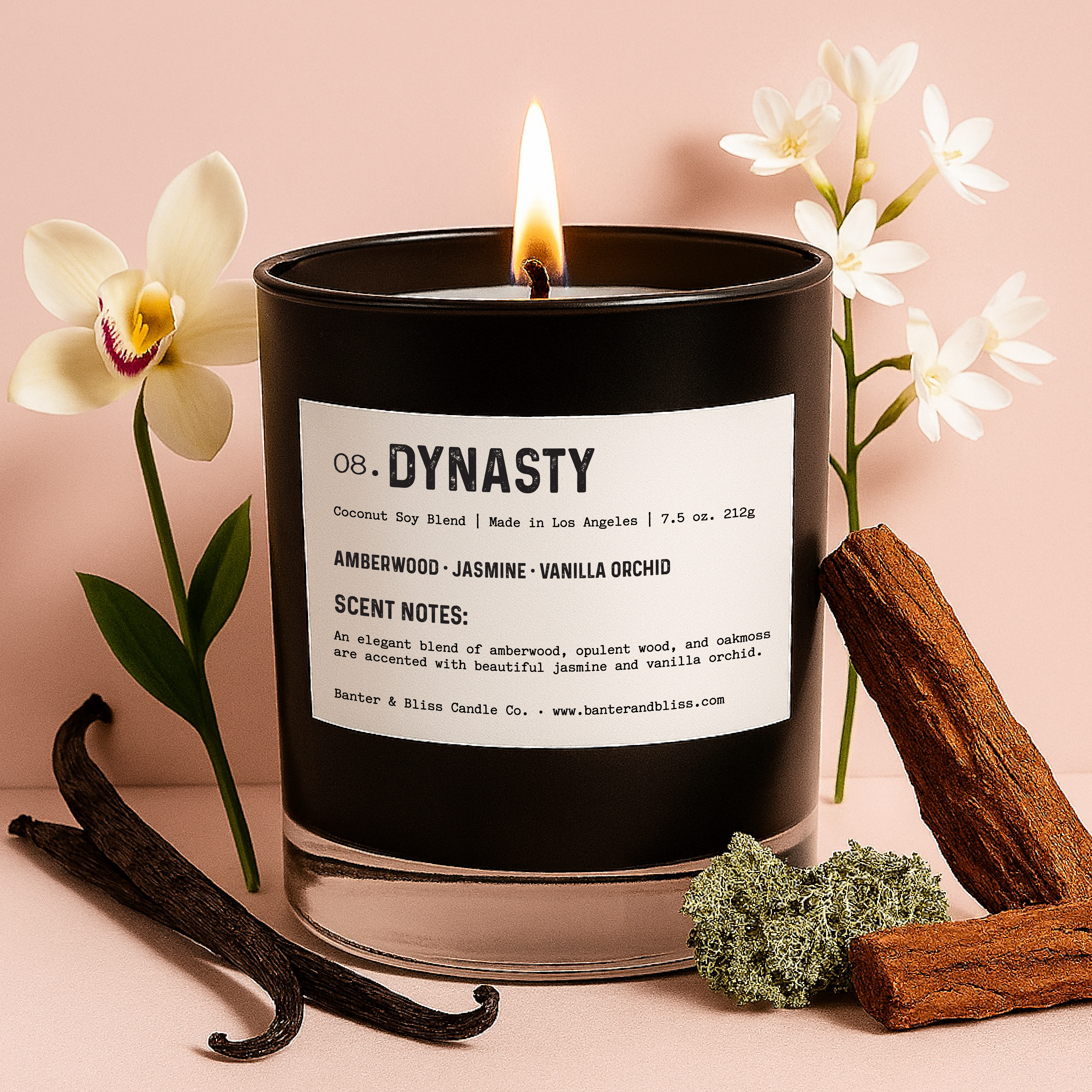 Dynasty candle by Banter & Bliss Candle Co. with notes of amberwood, jasmine, and vanilla orchid, shown lit and styled with natural scent ingredients on a pastel pink background.