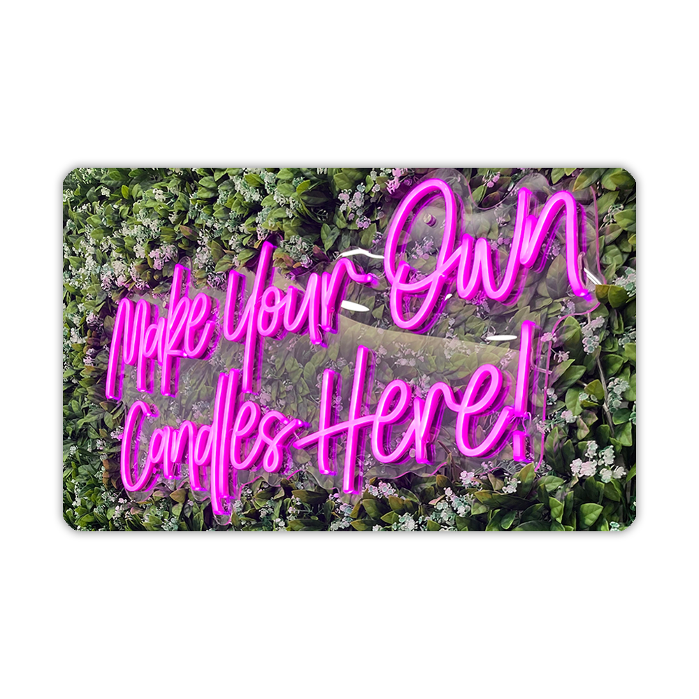 Neon sign with the text 'Make Your Own Candles Here!' set against a foliage background.