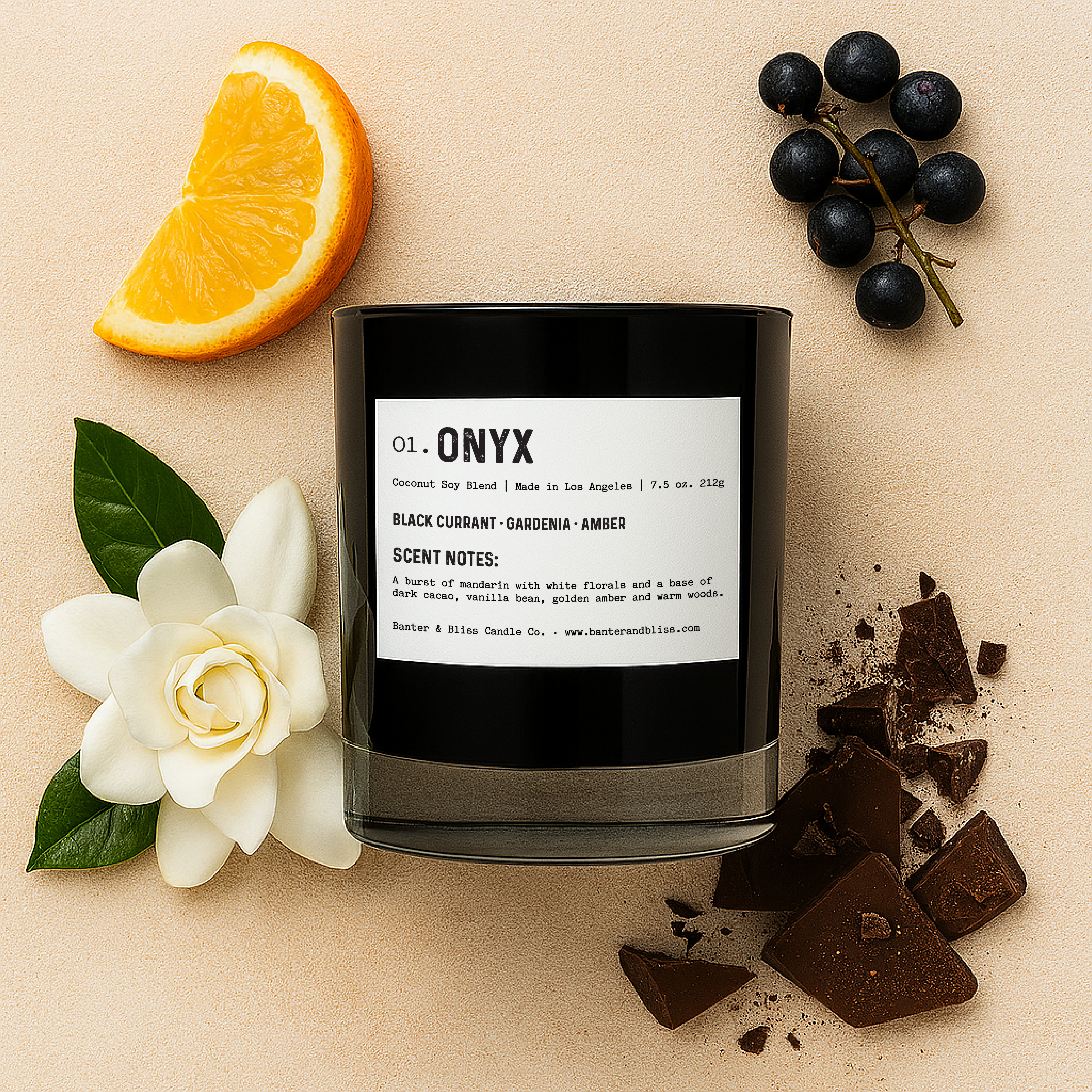 Flatlay of Banter & Bliss "Onyx" candle in black glass jar with white label, surrounded by mandarin orange slice, black currants, white gardenia flower, and dark cacao chunks on a pastel beige background — featuring scent notes of black currant, gardenia, amber, vanilla bean, and creamy sandalwood.