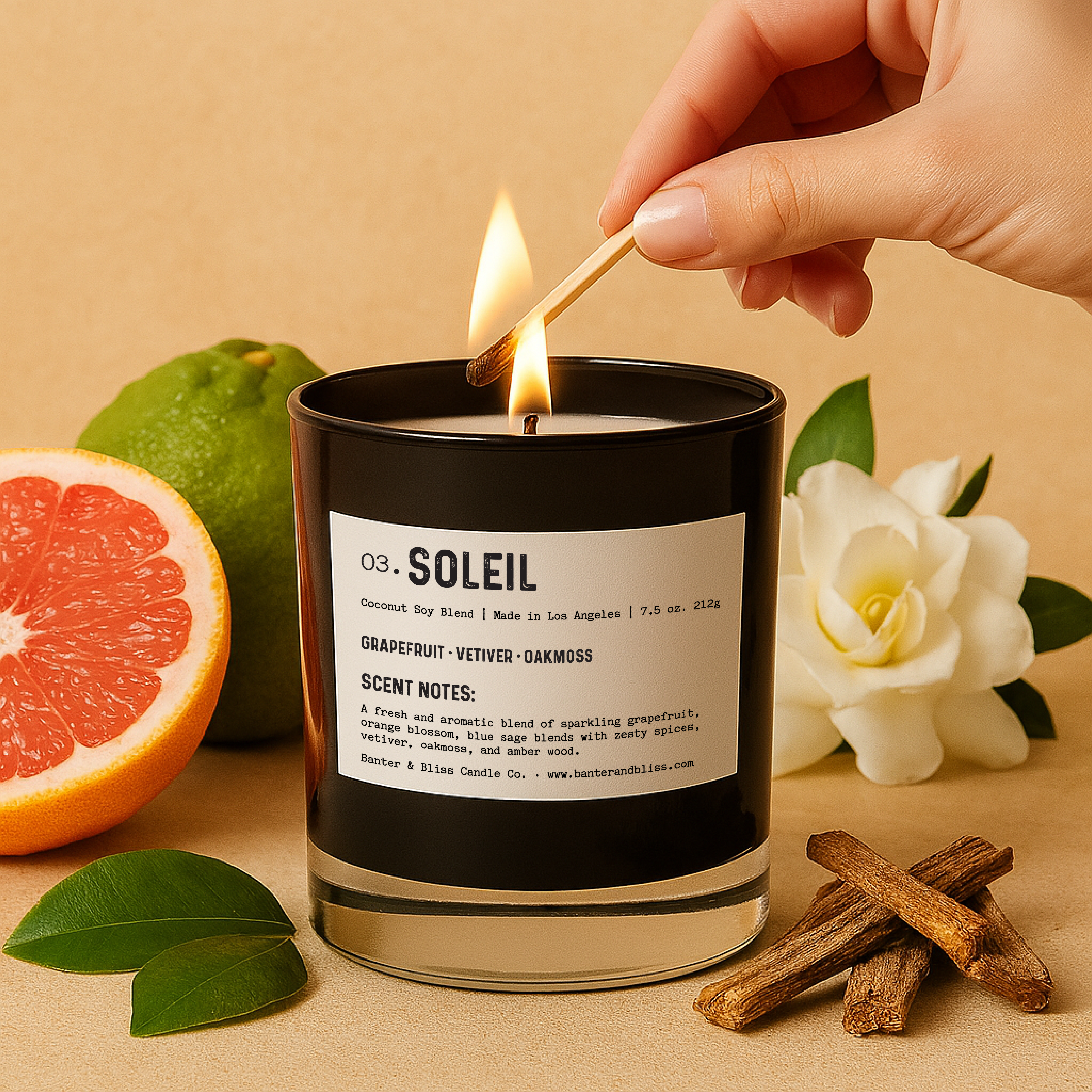 Banter & Bliss "Soleil" candle being lit with a match, surrounded by grapefruit, bergamot, white florals, green leaves, and dry wood on a pastel beige background — featuring scent notes of grapefruit, vetiver, oakmoss, orange blossom, blue sage, and amber wood.